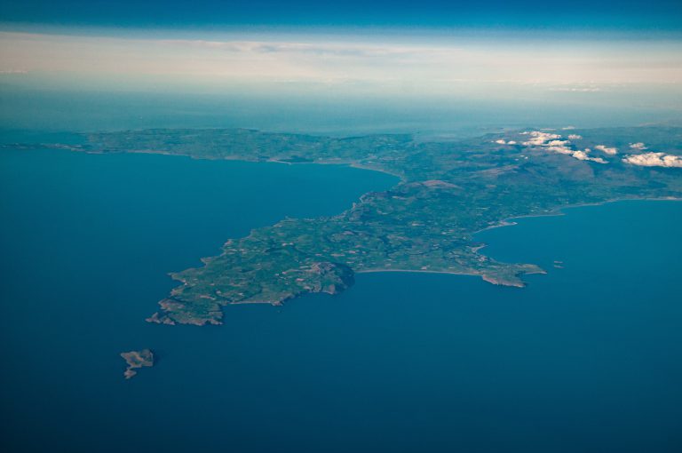 Wide aerial view of the peninsula at the northern end of Cardigan Bay in Wales with snow-covered Snowdonia in the distance and a full horizon